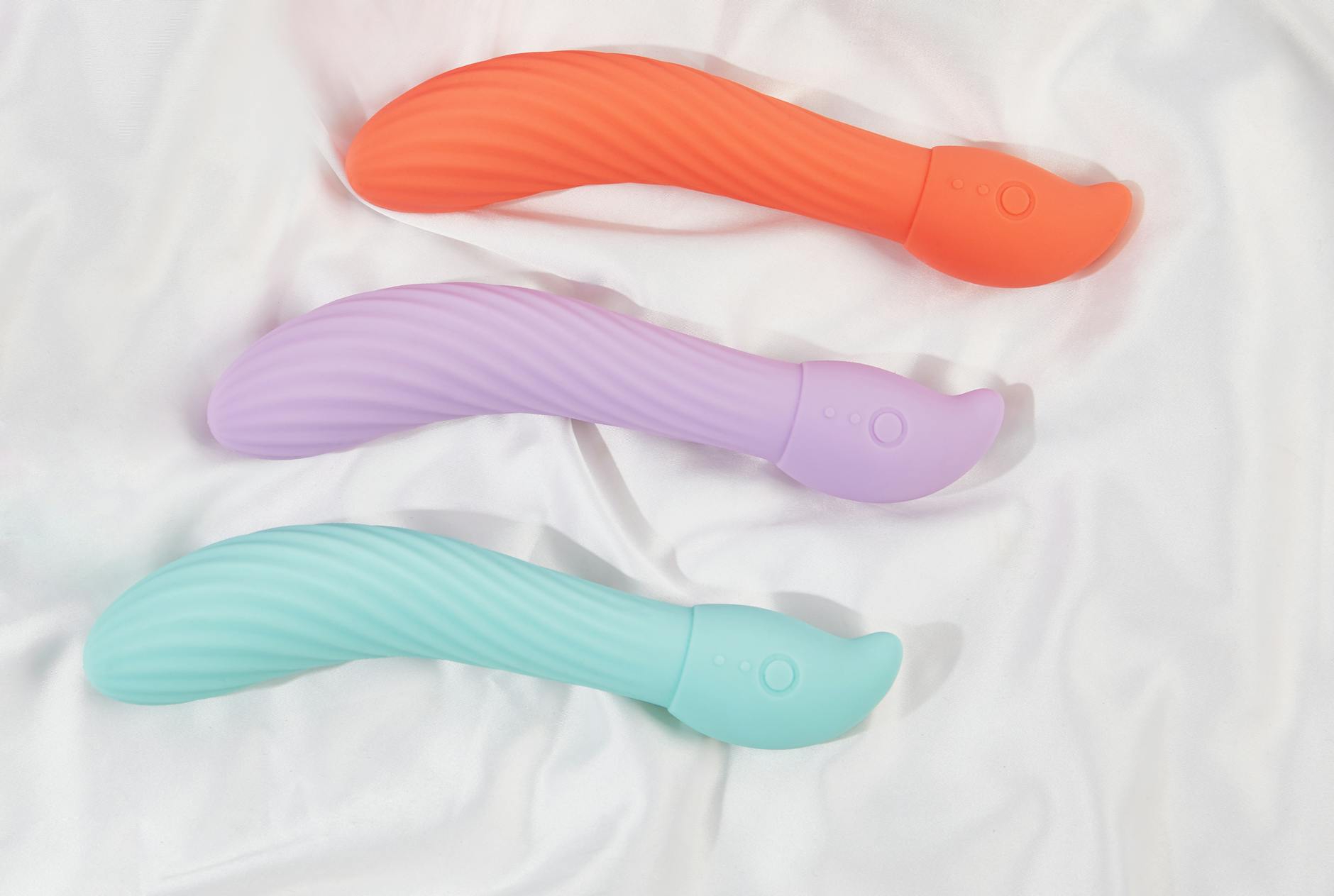 Three colorful suction vibrators arranged on white fabric, highlighting smooth design and texture.