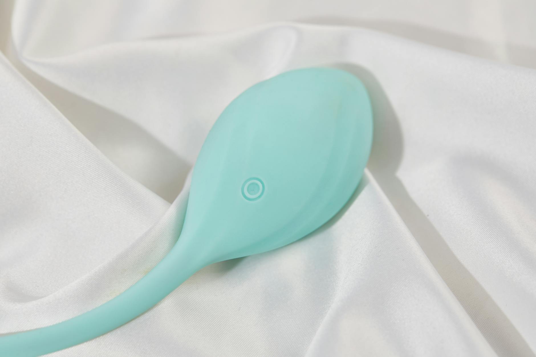 A stylish teal vibrator on smooth white silk fabric, symbolizing post-recovery intimacy.