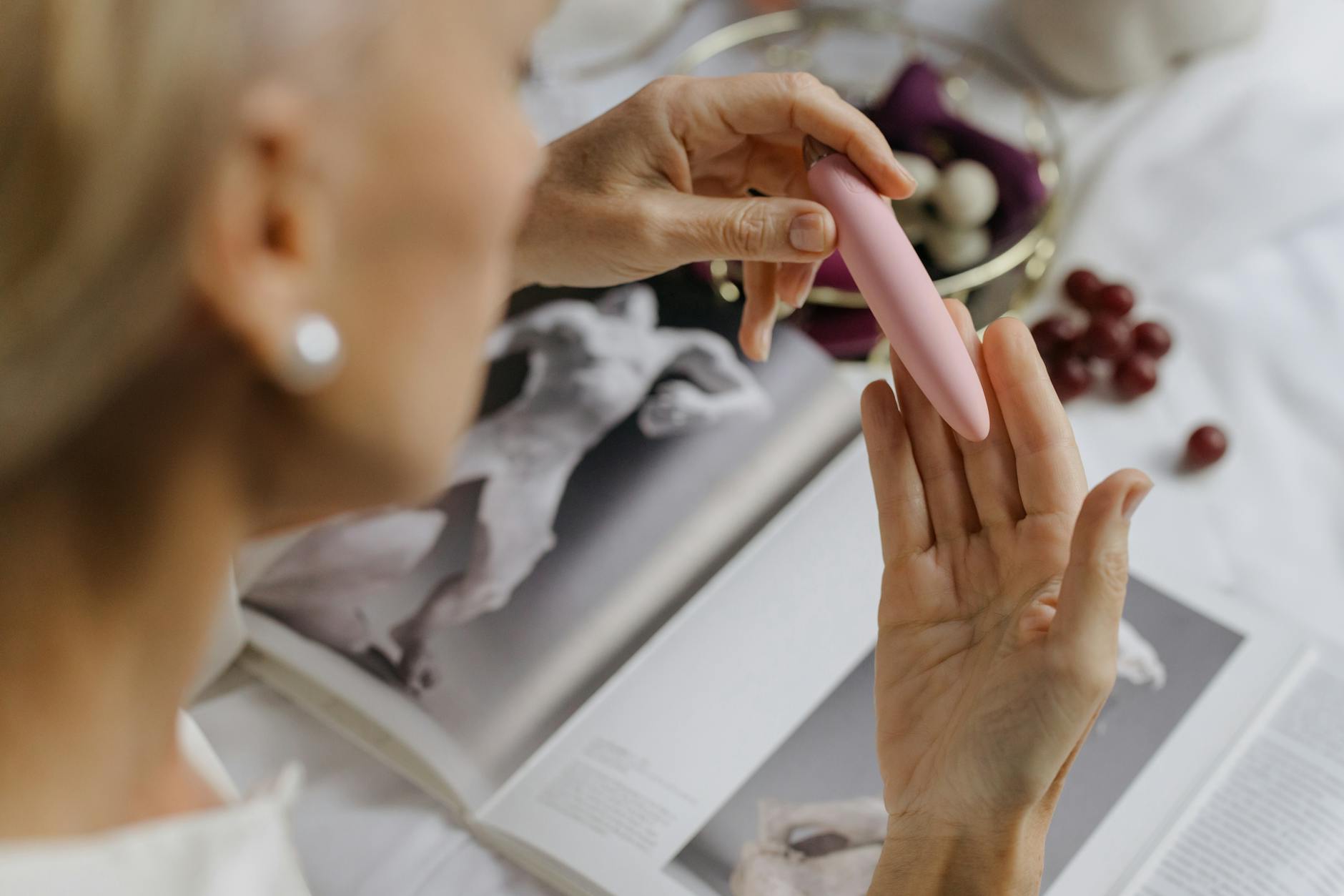 Close-up of a woman holding a pink vibrator with art books in the background, illustrating intimate self-pleasure