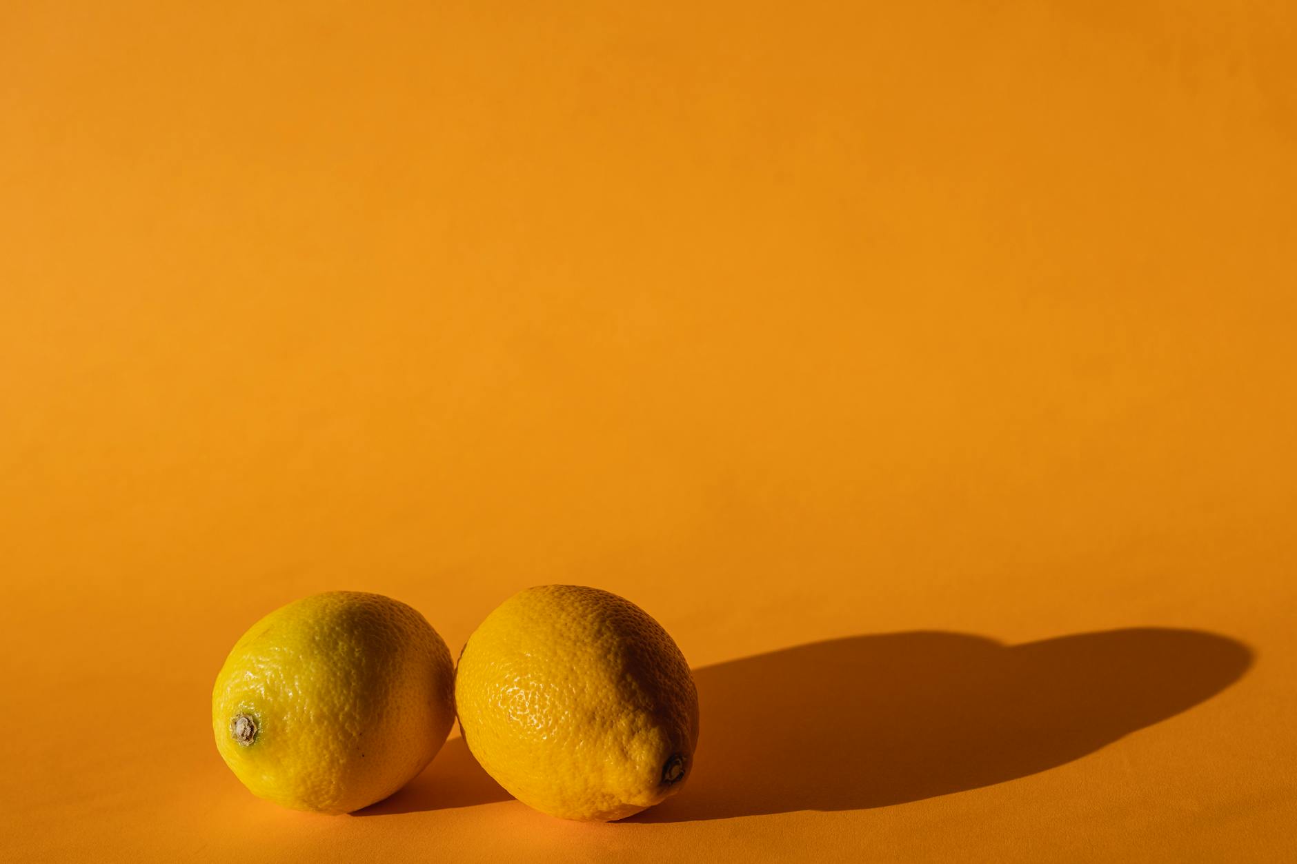 Close-up of a hand holding a lemon against a vivid yellow background